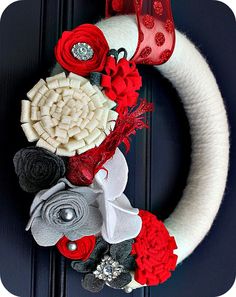 a white wreath with red and black flowers on the front door is adorned with ribbon