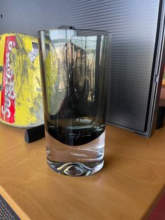 a glass sitting on top of a wooden table next to a computer monitor and keyboard