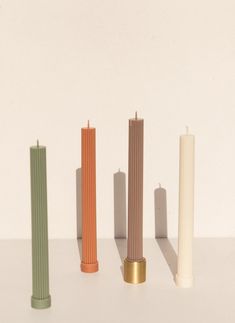 four different colored candles are lined up in a row on a white surface with one candle standing out from the others