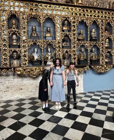 three people are standing in front of a wall with many busturines on it