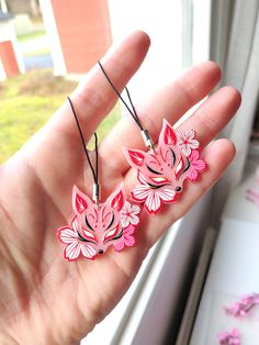 a hand holding three pink flowers in front of a window