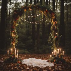 a wedding arch decorated with greenery and lit candles in the middle of a forest