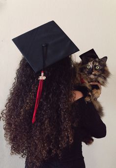 a woman wearing a graduation cap and holding a cat in her arms while she wears a black gown