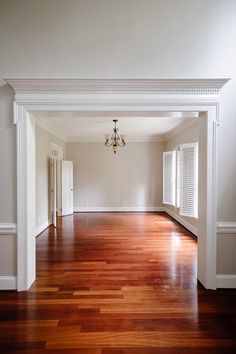 an empty living room with hard wood floors and white trim on the walls, along with a chandelier