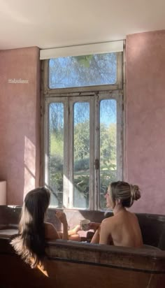 two women sitting in a bathtub looking out the window