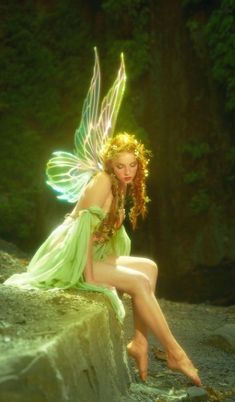 a woman dressed as a fairy sitting on a rock