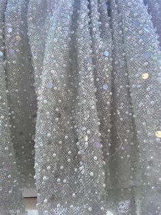 Beaded glitter net fabric for bridal gown. This is a beautiful rich fabric for wedding dress , wedding skirt. The color of the base is light grey or silver grey it has translucent glitters and subtle iridescent glitters. The base is net tulle covered with clear and iridescent glitter.  It is beaded on top with pearls beads and clear sequins. Sparkling Sequin Tulle Fabric For Evening, Sparkling Tulle Sequin Fabric For Prom, Prom Glitter Tulle Sequin Fabric, Tulle Sequin Fabric For Prom, Embellished Sequin Tulle Fabric For Prom, Prom Glitter Tulle Fabric With Sequins, Glamorous Sequined Tulle Fabric For Wedding, Glamorous Wedding Tulle Fabric With Sequins, Evening Glitter Tulle Fabric With Sequins