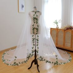 a white wedding dress on display in front of a window with greenery around it