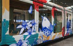 a colorful train with blue and white flowers painted on it's side is parked in a station