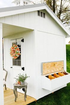 a small white shed sitting on top of a grass covered field next to a wooden floor