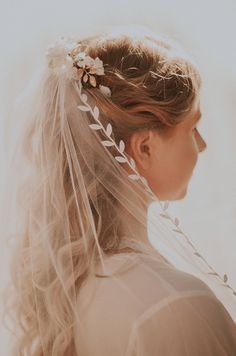 a woman wearing a veil with flowers on it's head and her hair in the wind