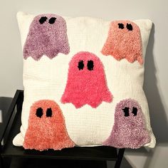 a decorative pillow with four ghost faces on it, sitting on a chair in front of a wall