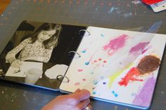 a child's hand is holding an open book with pictures on it and the pages are covered in paint