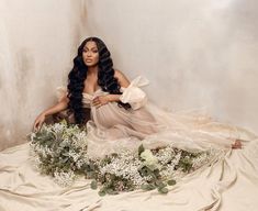 a woman sitting on top of a white sheet next to flowers and a teddy bear