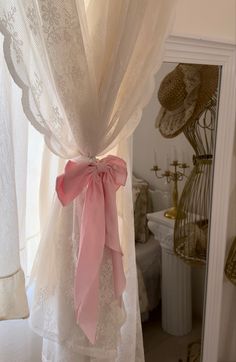 a pink ribbon tied to the back of a white curtain in a room with lace curtains