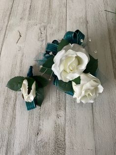 three white roses are placed on a wood floor with green leaves and ribbons around them