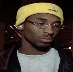 a young man wearing glasses and a yellow knitted beanie looks at the camera