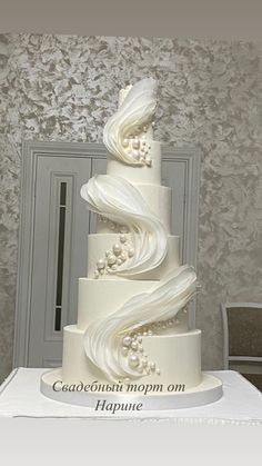 a three tiered white wedding cake sitting on top of a table in front of a wall