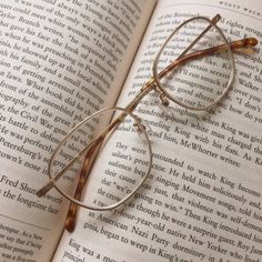 an open book with glasses resting on top of it's pages and reading glasses in the middle