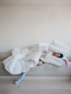 a woman laying on top of a white couch covered in pillows and blankets with her head under the covers