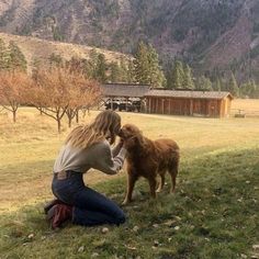 a woman kneeling down next to a brown dog on top of a grass covered field