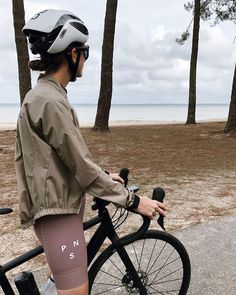 a woman in tights is standing next to her bike near the beach and trees