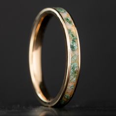 a gold wedding band with green and white marble inlays on it, against a black background