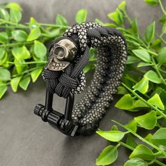 a black and white bracelet with a silver skull on it, sitting next to green leaves