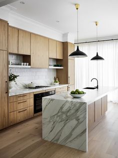 a kitchen with marble counter tops and wooden cabinets, along with black pendant lights hanging from the ceiling