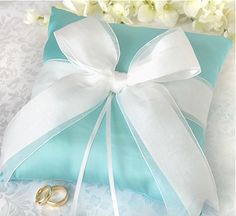 two wedding rings in a blue gift box with white ribbon and bow on it, sitting next to a bouquet of flowers