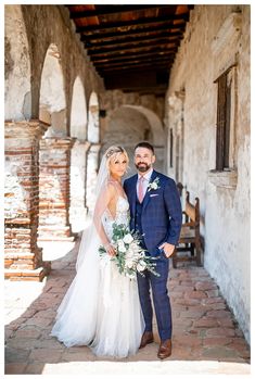 a bride and groom pose for a photo in an alleyway with stone arches on either side