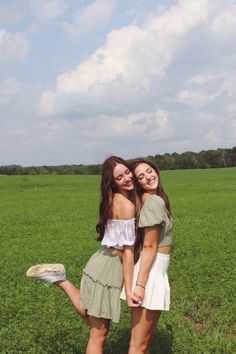 two young women standing next to each other in a field