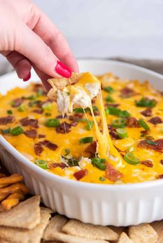 a hand holding a tortilla chip and dipping it into a casserole