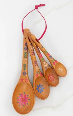 four wooden spoons with painted designs on them hanging from a string, against a white background