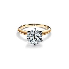 a yellow gold engagement ring with a round brilliant cut diamond in the center, on a white background