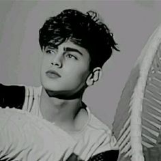 a young man holding a tennis racquet on top of a white wall in black and white