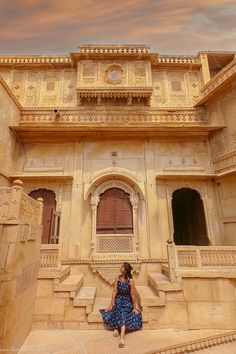 a woman in a blue dress is sitting on the steps outside an old building with intricate carvings