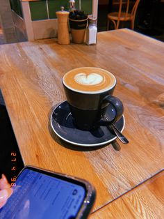 a cup of coffee sitting on top of a wooden table next to a cell phone