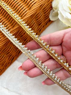 a hand holding two gold bracelets on top of a table next to a basket