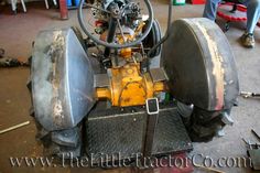 an old yellow tractor sitting on top of a piece of metal in a garage next to other tools