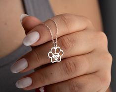 a woman's hand holding a silver dog paw necklace