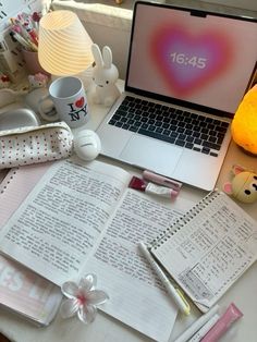 a laptop computer sitting on top of a desk next to an open book and cup