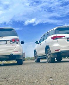 two white suvs are parked on the side of the road in front of a blue sky