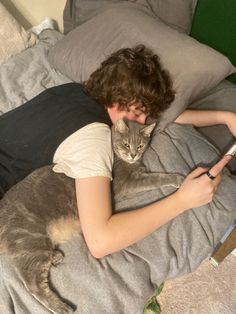 a person laying in bed with a cat on their lap and looking at a cell phone