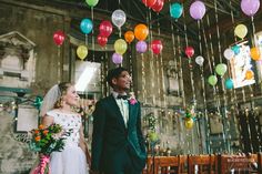 a bride and groom are standing under balloons