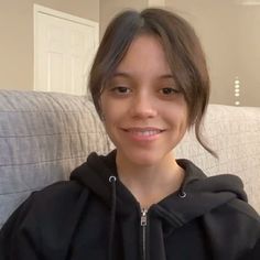 a woman sitting on a couch wearing a black hoodie and smiling at the camera