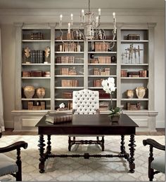 a living room filled with furniture and a chandelier above a table in front of bookshelves