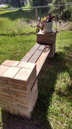 a wooden bench made out of bricks sitting in the grass next to a potted plant