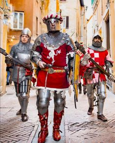 three men dressed in medieval armor are walking down the street