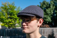 a young man wearing glasses and a crocheted newsboy hat looks off to the side